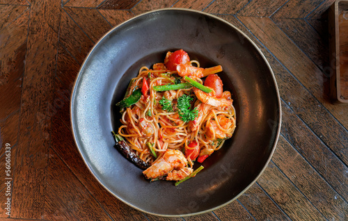 Directly above view, Italian pasta spaghetti with prawns in Tom Yum flavor, Thai style pasta, tasty and spicy, delicious menu in dark color plate on wooden table