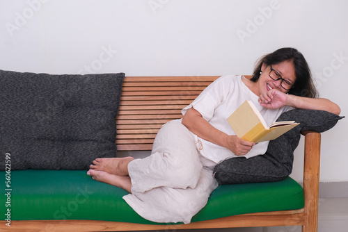 Asian woman enjoyed reading book casually lying on green sofa alone photo