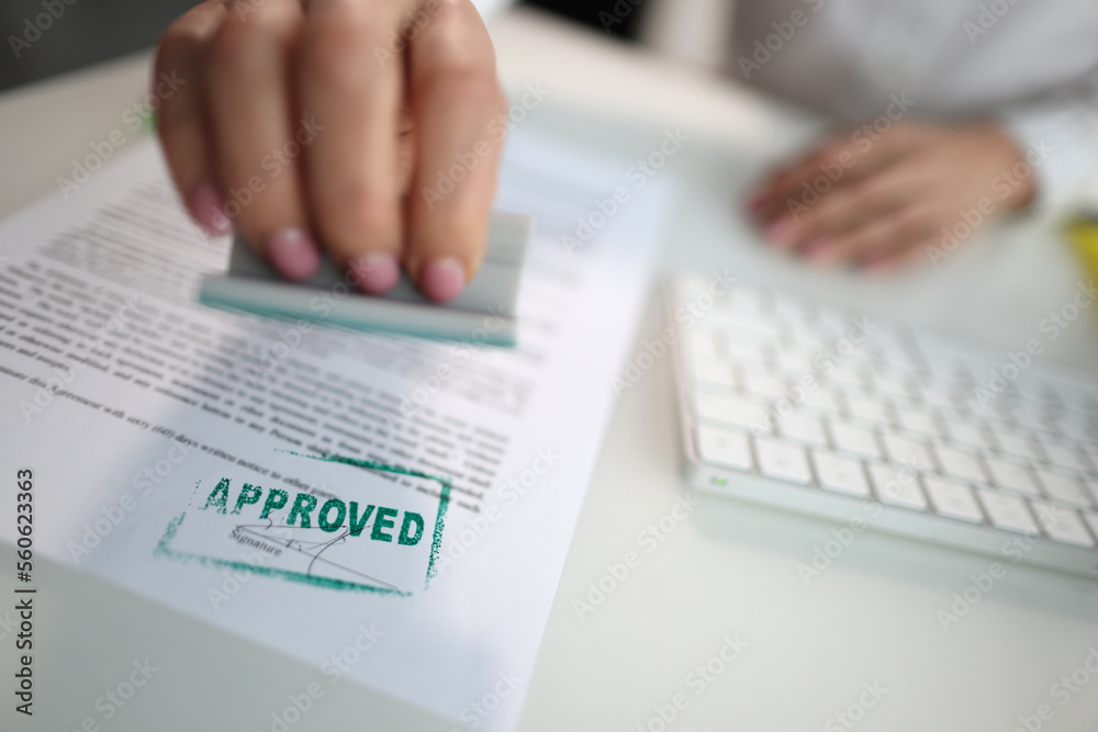 Fototapeta premium Closeup of a person hand stamping green approved seal on text approved document on table