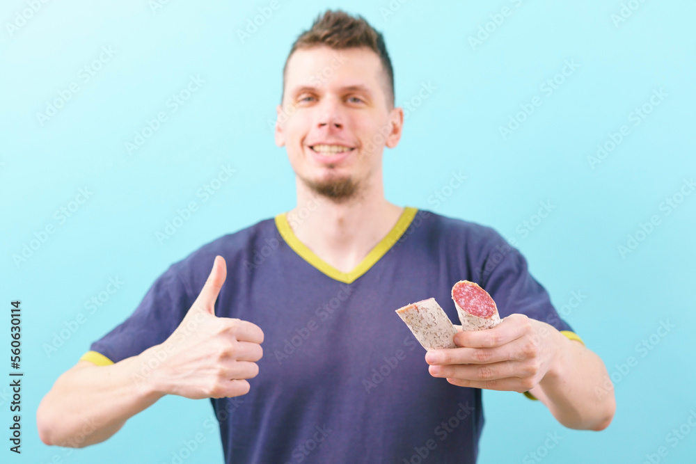 A smiling man holding a white cut Spanish sausage and shows thumb up on a blue background. Sausage. Spanish. Hand. Old. Background. Food. Spain. Thin. Buffet. Fat. Tripe. Pork A smiling man holding a white cut Spanish sausage and shows thumb up on a blue background. Sausage. Spanish. Hand. Old. Background. Food. Spain. Thin. Buffet. Fat. Tripe. Pork