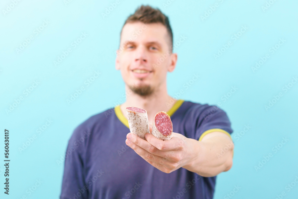 A smiling man holding a white cut Spanish sausage and gives it to the camera on a blue background. Sausage. Spanish. Hand. Old. Background. Food. Spain. Thin. Buffet. Fat. Tripe. Pork A smiling man holding a white cut Spanish sausage and gives it to the camera on a blue background. Sausage. Spanish. Hand. Old. Background. Food. Spain. Thin. Buffet. Fat. Tripe. Pork
