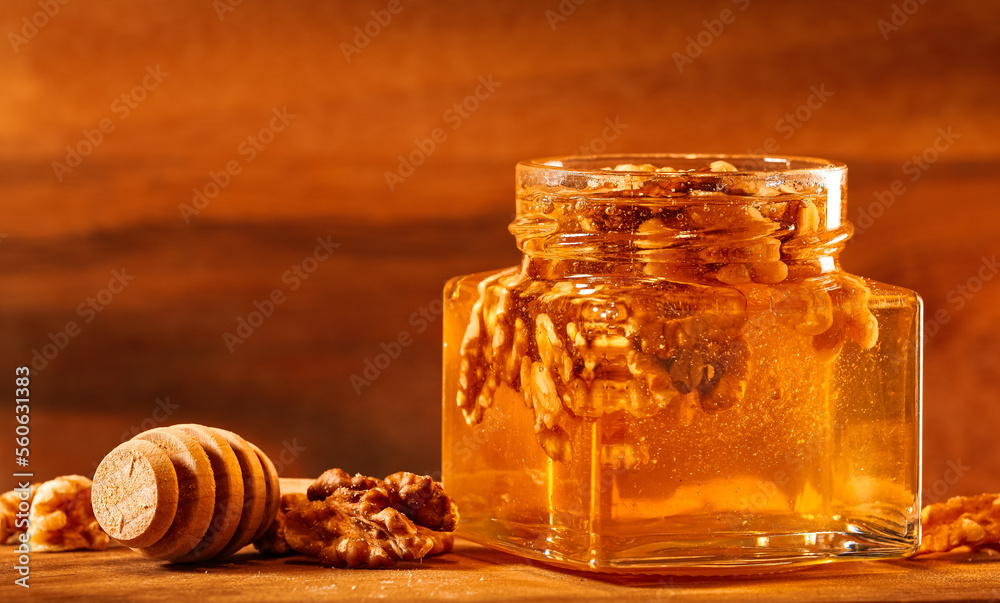 Glass jar with honey mixed with nuts photographed on a wooden table, honey dipper next to it, against wood background. Healthy breakfast snack.
