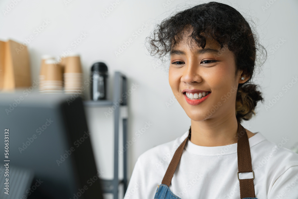 Happy young Asian woman cashier wears an apron and using pos terminal to input orders on coffee shop counter. Happy young Asian woman cashier wears an apron and using pos terminal to input orders on coffee shop counter.