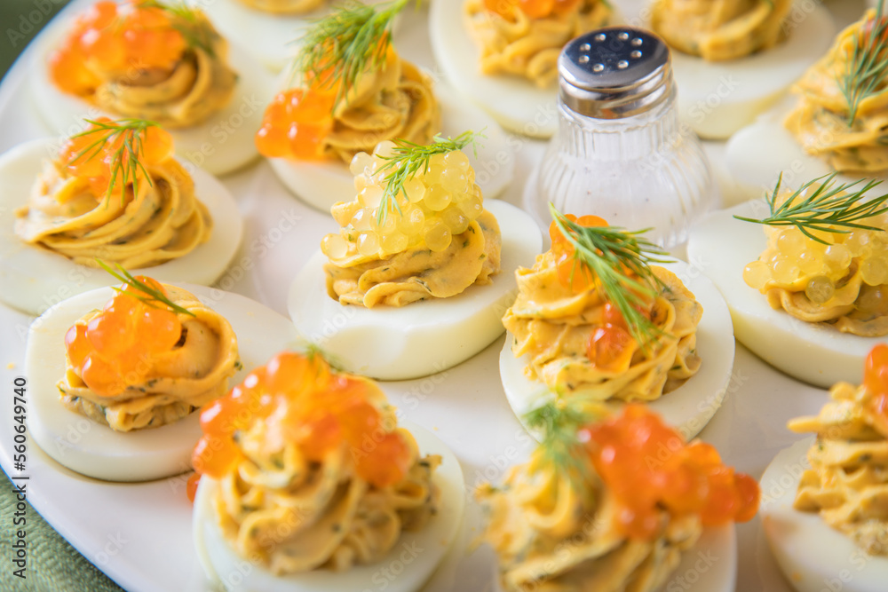 Gefüllte teuflische russische Eier mit Dill und orange Keta Lachs und gelb Saibling Kaviar auf Eierteller, Serviette grün, Silber Teller und Pastell Pink Rosa Hintergrund Gefüllte teuflische russische Eier mit Dill und orange Keta Lachs und gelb Saibling Kaviar auf Eierteller, Serviette grün, Silber Teller und Pastell Pink Rosa Hintergrund