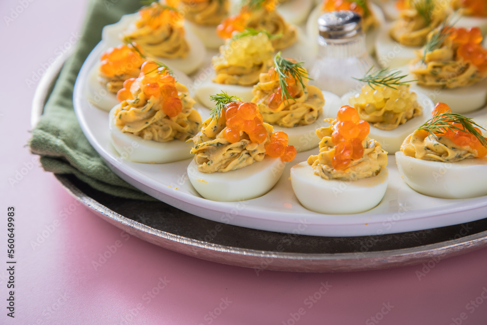 Gefüllte teuflische russische Eier mit Dill und orange Keta Lachs und gelb Saibling Kaviar auf Eierteller, Serviette grün, Silber Teller und Pastell Pink Rosa Hintergrund Gefüllte teuflische russische Eier mit Dill und orange Keta Lachs und gelb Saibling Kaviar auf Eierteller, Serviette grün, Silber Teller und Pastell Pink Rosa Hintergrund