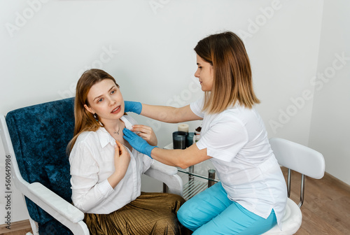 Beautician examining face skin of female patient. Consultation in cosmetology clinic. Female professional beauty doctor talking with pretty young female. Doctor listening carefully