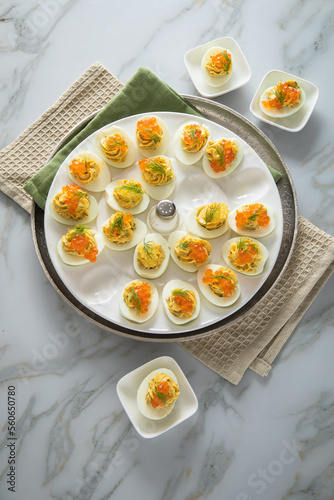 Gefüllte teuflische russische Eier mit Dill und orange Keta Lachs und gelb Saibling Kaviar auf Eierteller, Serviette grün, Silber Teller und Marmor Hintergrund hell