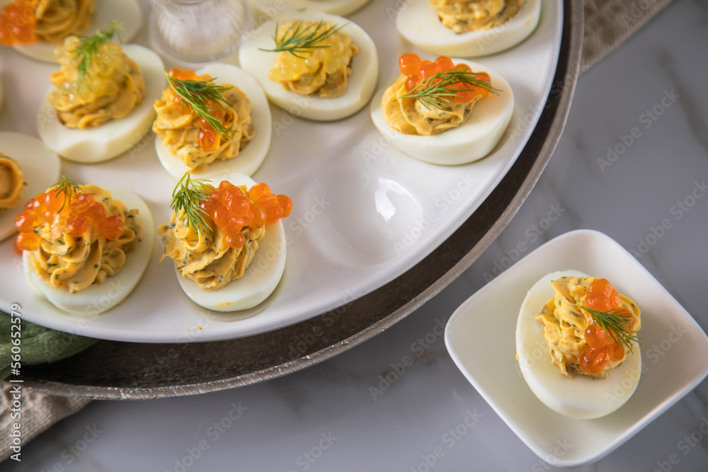 Gefüllte teuflische russische Eier mit Dill und orange Keta Lachs und gelb Saibling Kaviar auf Eierteller, Serviette grün, Silber Teller und Marmor Hintergrund hell Gefüllte teuflische russische Eier mit Dill und orange Keta Lachs und gelb Saibling Kaviar auf Eierteller, Serviette grün, Silber Teller und Marmor Hintergrund hell