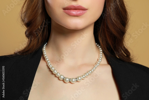 Young woman with elegant pearl necklace on brown background, closeup