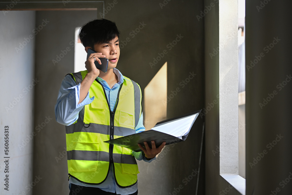 Handsome asian male inspector talking on mobile phone and working at construction site Handsome asian male inspector talking on mobile phone and working at construction site