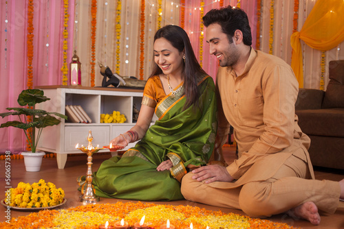 Young couple decorating their house on Diwali and lighting Diyas together - Hindu festival custom. Stock image of an Indian husband-wife in traditional outfits lighting diyas and making rangoli tog... photo