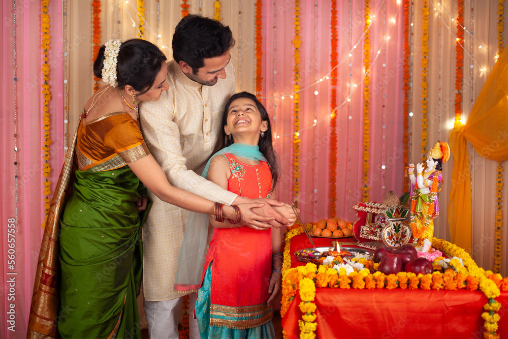 A happy Indian family is celebrating Krishna Janmashtami - Father. mother and daughter. Stock image of mother and father helping their daughter in offering prayer to Ladoo Gopal for Krishna Puja - ...