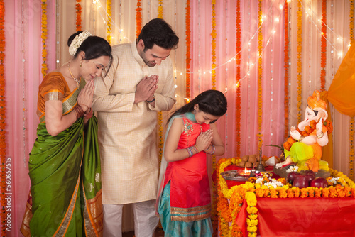 Spiritual Indian family with folded hands praying to Lord Ganesha idol - Festival. Royalty free image of a family dressed in Indian dress - Cultural show by bowing their heads to pray during Ganesh... photo