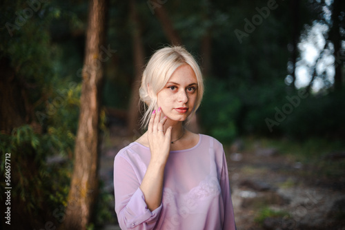 Blonde girl on a summer day on the shore near the river in nature in a dress