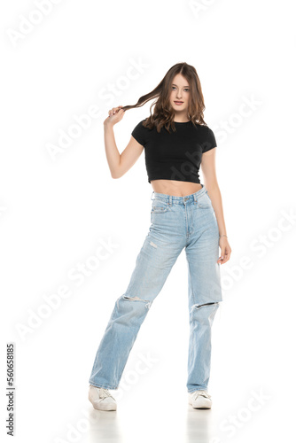 Young female model wearing ripped jeans and black shirt posing on a white background. Front view