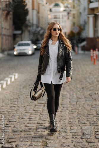 Fashionable blonde woman model with black leather jacket and style sunglasses walking the city street