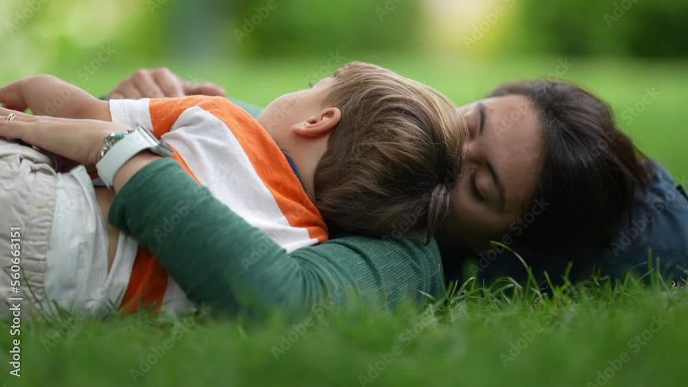 Mother lay on grass with child son. Parenting love and care. Mom laying outdoors with baby toddler Mother lay on grass with child son. Parenting love and care. Mom laying outdoors with baby toddler