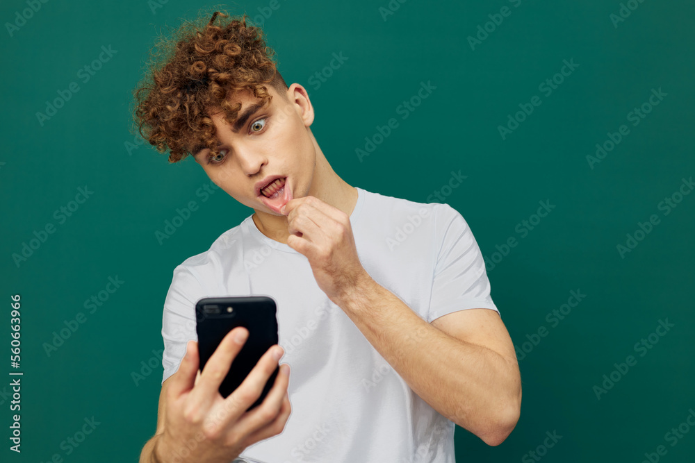 a funny man with curly hair stands on a green background in a gray T-shirt and holds his hand near his mouth, holding the phone in his hand looking into it a funny man with curly hair stands on a green background in a gray T-shirt and holds his hand near his mouth, holding the phone in his hand looking into it