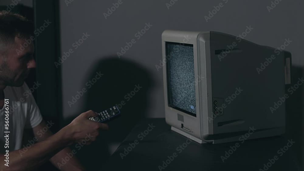 Broken Television or TV Propaganda. Mind Control - Zombified Man in White T-shirt Switches Channels on the Old TV in Dark Room. TV Signal Search. Distortion on the Screen. Medium Close-Up, Film Grain