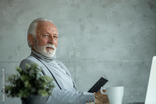 Quadro em tela Senior businessman working in his office and holding a notebook while looking at