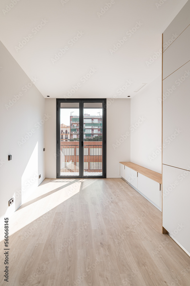 Direct view of black metal framed glass sliding doors at end of an empty bright clean room. Doors leading to spacious balcony overlooking neighboring house. Sunlight enters through glass door. Direct view of black metal framed glass sliding doors at end of an empty bright clean room. Doors leading to spacious balcony overlooking neighboring house. Sunlight enters through glass door.