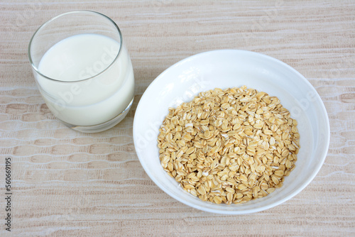 oatmeal flakes in white bowl isolated with glass of milk on beige background, close-up