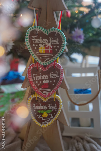Christmas food. Colorful Christmas handmade gingerbread in the shape of heart hangs on wooden tree close-up. Behind Christmas decor. Christmas cozy atmosphere. Selective focus.