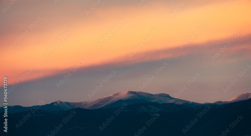 Stunning sunset with beautiful shades of orange, pink, purple and blue colors with the silhouette of a mountain range. Wallpaper, natural background with copy space.
