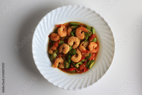 Chili prawns or Sambal Udang with petai or pete or mlanding (Parkia speciosa) cooked with mashed red chili and tomato in white plate, isolated on white background. Indonesia cuisine food, top view.