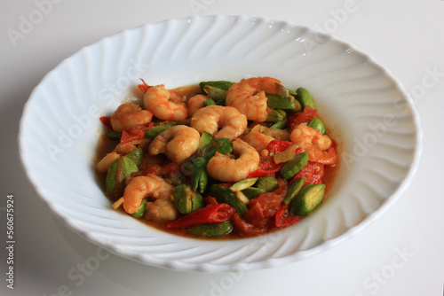 Chili prawns or Sambal Udang with petai or pete or mlanding (Parkia speciosa) cooked with mashed red chili and tomato in white plate, isolated on white background. Indonesia cuisine food.