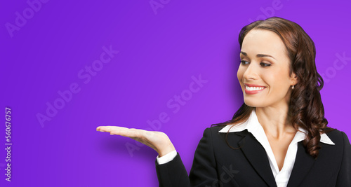 Portrait image of happy smiling business woman in black confident suit showing, giving, holding, advertising, isolated over violet background. Executive office worker, teacher or real estate agent.