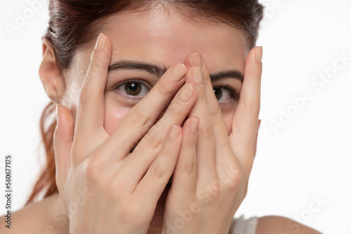 Portrait of yong happy ashamed woman, covering face with hands, beautiful model posing in studio over white background