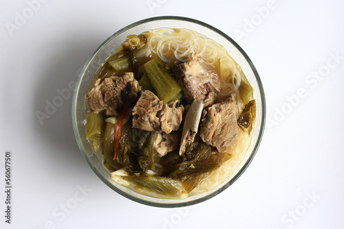 sup bakut or baikut babi sayur asin, is popular Chinese Indonesian pork rib soup with pickled cabbage or mustard greens and vermicelli in clear bowl, isolated on white background, top view.