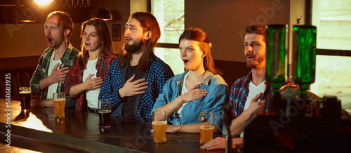 Φωτογραφία Group of young people, men and women meeting at pub to watch sport match translation