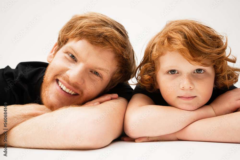 cheerful young man with redhead son lying with crossed arms on light grey background. cheerful young man with redhead son lying with crossed arms on light grey background.
