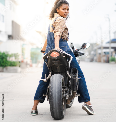 Multiracial woman motorcycle biker sitting on a sport motorbike. Portrait of beautiful female model posing on motor vehicle looking at camera. Girl rider freedom adventure lifestyle.