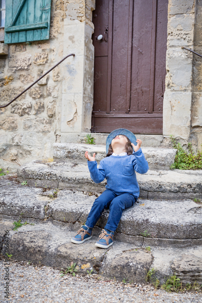 Little handsome baby boy sitting on ancient stone stairs and playing outdoor with straw hat in old city Little handsome baby boy sitting on ancient stone stairs and playing outdoor with straw hat in old city
