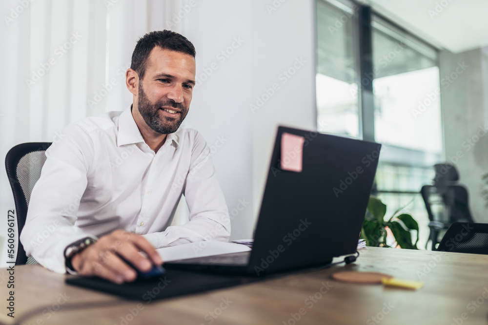 Portrait of young business man sitting at his desk in the office using laptop Portrait of young business man sitting at his desk in the office using laptop