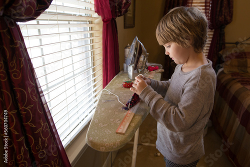 Young boy at ironing board with sewing items around him photo