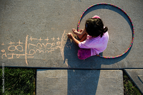 Girl with hula hood on driveway writing chalk numbers photo