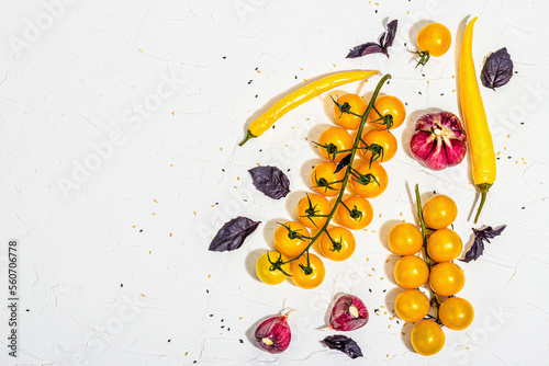 Culinary background with ripe vegetables. Yellow tomato cherries, chili pepper, garlic, purple basil. Fresh vegetables on white putty background, modern hard light, dark shadow, flat lay photo