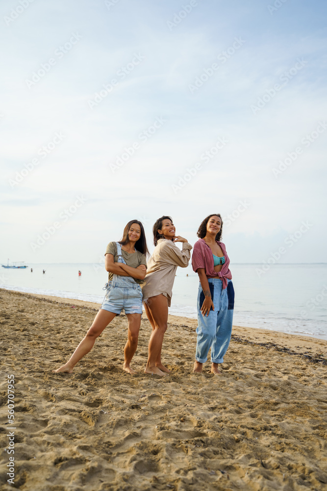 Female friends posing on sea shore at beach with sky in background Female friends posing on sea shore at beach with sky in background