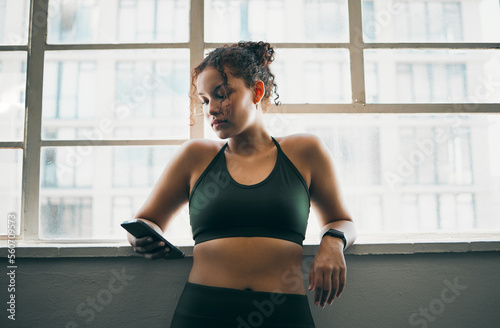 Idea, phone and exercise with a sports woman by a window, standing in the gym during a fitnesss workout. Health, thinking and a female athlete using social media or an app to track her training photo