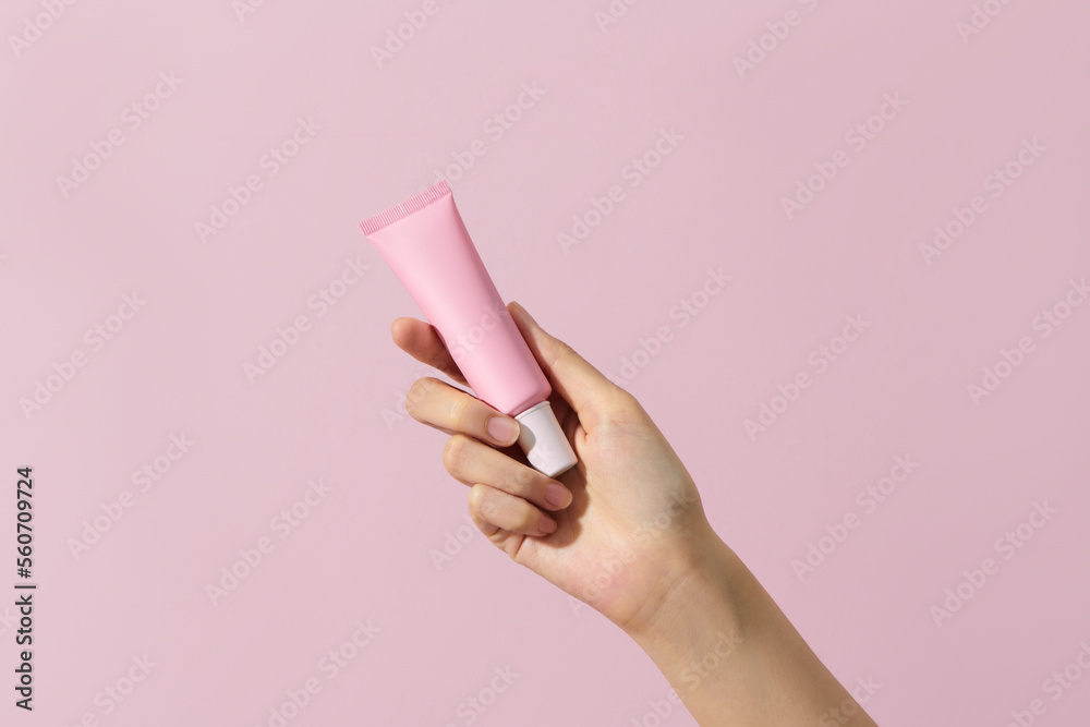 Hand holding a pink tube, isolated on pink background