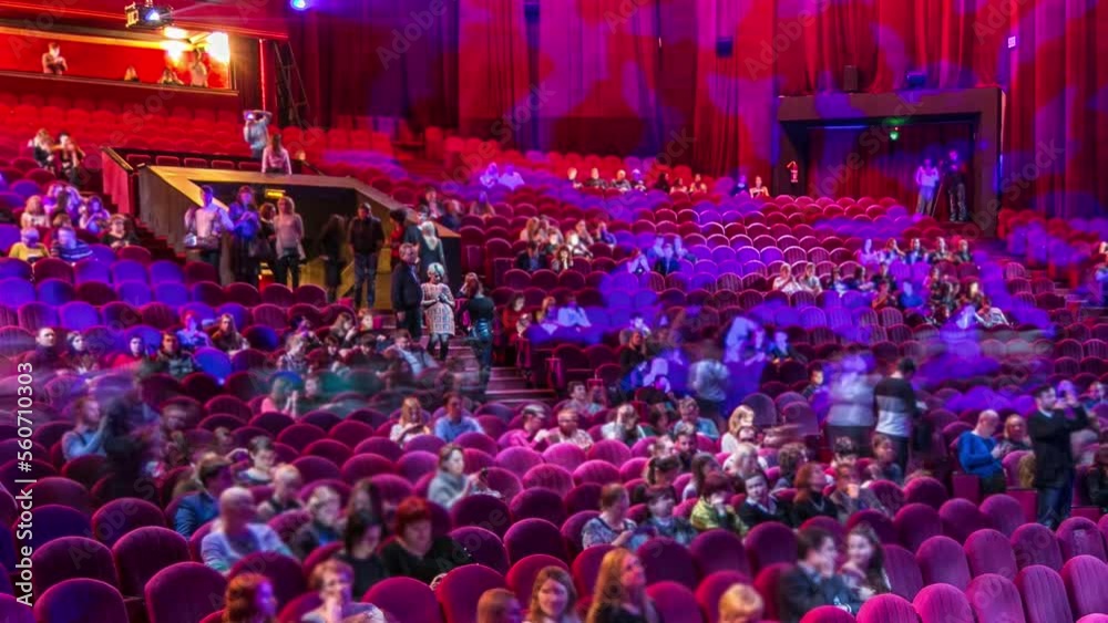 Spectators gather in the auditorium and watch the show in theatre timelapse. Large hall with red armchairs seats. Viewers filling places until turn off the light. View from left side