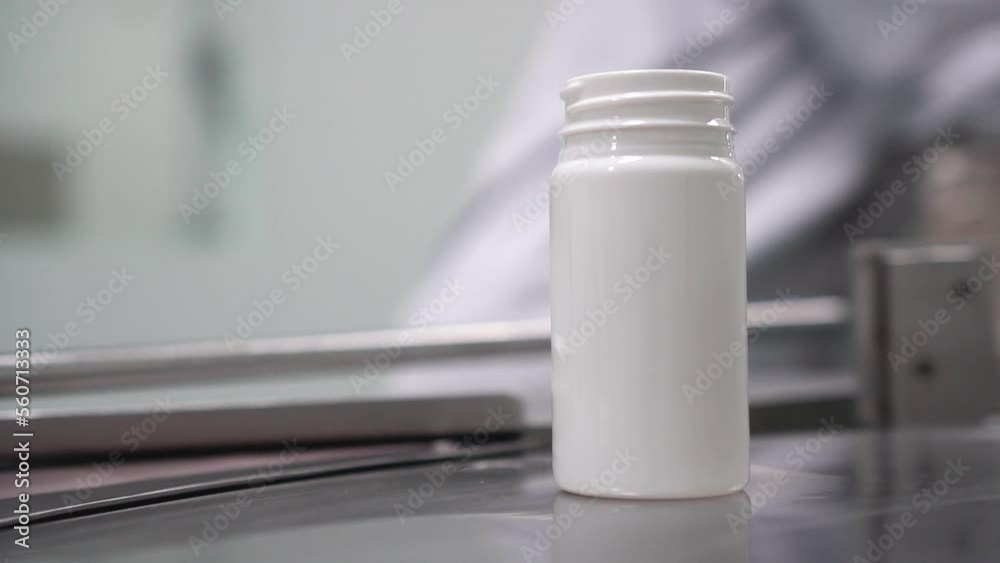 Envasado de medicamentos farmacéuticos en recipiente de color blanco sobre un cinta giratoria para industria farmacéutica.