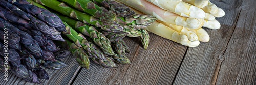 Raw white, purple, green asparagus on wooden background. Healthy food concept, place for copy space. The vegetable is rich in fiber, a natural prebiotic.