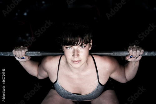 Strong female does a squat with a bar in a fitness gym photo