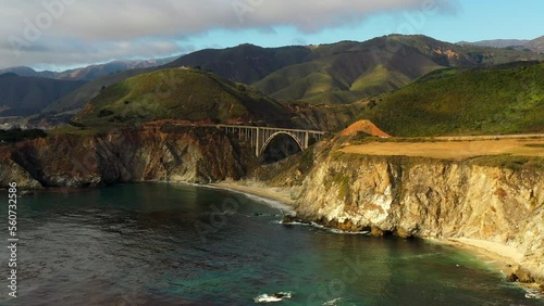 Aerial Panning Shot Of Bixby Creek Bridge Amidst Rock Formations, Drone Flying Over Sea Under Clouds - San Francisco, California photo