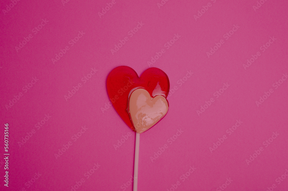 The lollipop is in the shape of two hearts - red and white against the background of the color of the viva magenta. Holiday. Valentine's Day. March 8. Postcard for the holiday.